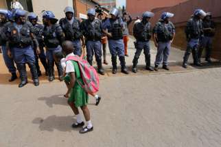 School children walk past a line of police officers during protests against the cost of higher education in Johannesburg, South Africa, Oct. 12. After chaos broke out in a Catholic church as it hosted a meeting to resolve a university crisis, South Africa&#039;s Jesuits said the church would no longer be open for these talks.