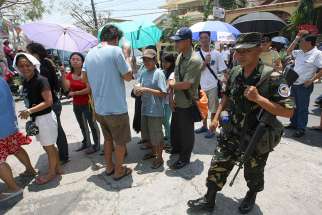 A Philippine air force trooper walks past voters lining up outside a precinct on election day in 2010 in Las Pinas. Archbishop Socrates Villegas of Lingayen-Dagupan is urging Catholics to heed the Ten Commandments before they head to the polls in May to vote for offices ranging from president to local village councillors.