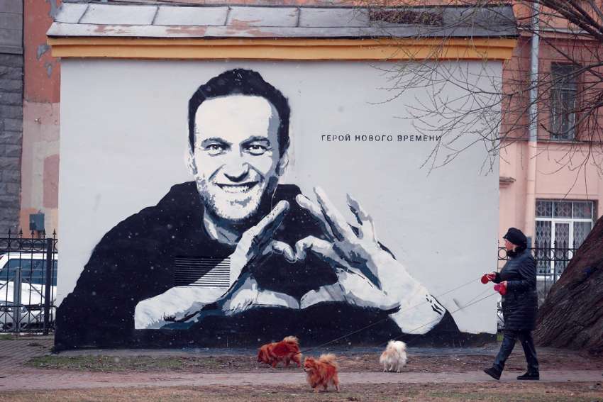 A woman walks her dogs in front of an image of Russian politician Alexei Navalny in St. Petersburg, Russia, April 28, 2021.