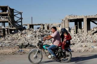  Motorists are pictured in a file photo riding a motorcycle past ruins of buildings destroyed during fighting in Kobani, Syria. Ambassadors to the Vatican from around the world were called together Oct. 15, 2020, to hear from Cardinal Mario Zenari, apostolic nuncio to Syria, about the humanitarian disaster there.