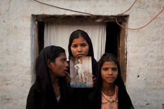 The daughters of Asia Bibi pose in 2010 with an image of their mother while standing outside their residence in Sheikhupura, Pakistan. 