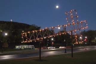 The fallen cross is lit up at night with Montreal’s landmark cross atop Mount Royal in the background.