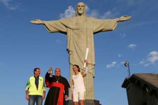Cardinal Orani Tempesta of Rio de Janeiro holds the Olympic flame Aug. 5 as Rio Mayor Eduardo Paes and former Brazilian volleyball player Isabel Barroso look on in front of the Christ the Redeemer statue.
