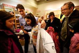 Canadian Prime Minister Justin Trudeau helps a young Syrian refugee try on a winter coat after she and others arrived Dec. 10, 2015 from Beirut at the Toronto Pearson International Airport.