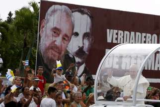 Pope Francis waves to people as he passes a billboard showing images of Cuba&#039;s former leader Fidel Castro and Cuban independence hero Jose Marti Sept. 19 in Havana.