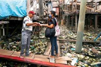 Liliane Tavares de Moura, 44, a parishioner of Our Lady of Perpetual Help Catholic Church in Manaus, Brazil, delivers a protective mask to a resident in one of the city’s slums.