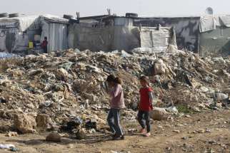 Syrian girls walk near garbage inside an informal refugee camp in Zahle, Lebanon. Lebanon continues to bear the brunt of absorbing massive numbers of refugees.