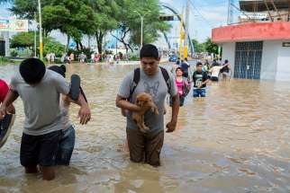 People cross a street flooded by the Piura River March 27 in Peru.
