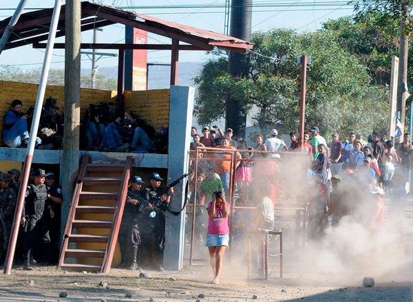 A woman shields herself as she walks near police officers who have taken cover after family members tried to enter a prison in Comayagua, Honduras, Feb. 15. A massive fire swept through the overcrowded prison in Honduras, killing hundreds, including many trapped inside their cells, officials said.