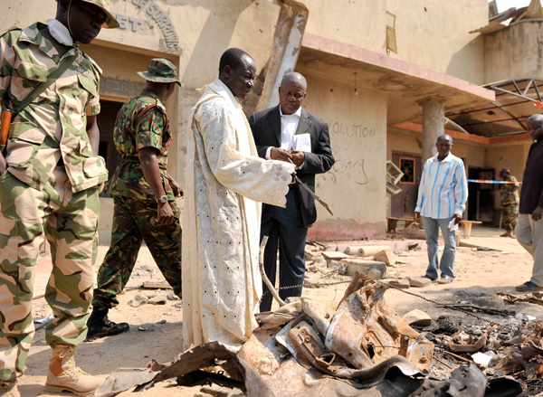 A priest and security forces look over the scene of a car bomb explosion at St. Theresa Catholic Church in Madalla, just outside Nigeria's capital Abuja, Dec. 25. 
