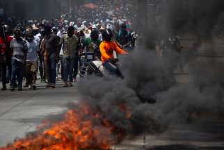 Demonstrators march past burning debris during a protest against the government of Haitian President Jovenel Moïse in Port-au-Prince March 28, 2021.