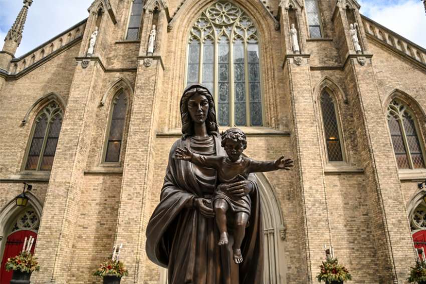 St. Michael&#039;s Cathedral in downtown Toronto is seen behind a statue of Mary with the Child Jesus.