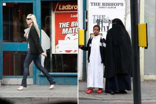 Right: a woman wearing a niqab stands by a light crossing with a boy. Left: a woman wearing sunglasses walks past a store.