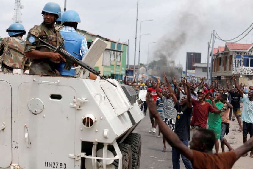 People chant slogans against Congolese President Joseph Kabila as armed U.N peacekeepers watch protesters Dec. 20 in Kinshasa.