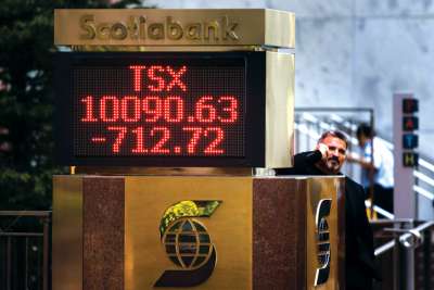 A man stands beside a sign indicating the Toronto Stock Exchange index in downtown Toronto in this CNS file photo.