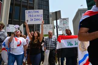 Protesters display signs and carry flags during an Aug. 1 protest in Detroit. More than 150 people protested the persecution of Christians in Iraq, calling on the U.S. government and others to step in to help those given an ultimatum to convert to Islam, pay a heavy tax or be killed in their homeland. 