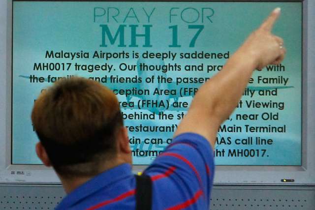 A bystander points in front of a &quot;Pray for MH17&quot; message on a flight information board at Malaysia&#039;s Kuala Lumpur International Airport July 18.  Catholics involved in the fight against HIV and AIDS took a few moments July 21 to remember their friends and colleagues who perished in the Malaysia Airlines flight shot down over eastern Ukraine.