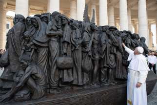 Pope Francis reaches out to the statue titled Angels Unawares by Canadian artist Timothy Schmalz at the Vatican last September. The statue depicts a group of migrants and refugees on a boat. Advocates are urging political leaders to include refugees and migrant workers in aid  support during the COVID-19 crisis.