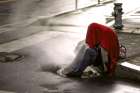 A homeless person finds warmth from steam emerging from a street vent.