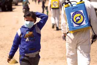 An internally displaced Syrian girl wearing a protective face mask walks as members of the Syrian Civil Defence force sanitize the Bab Al-Nour camp in Azaz to control the spread of COVID-19.