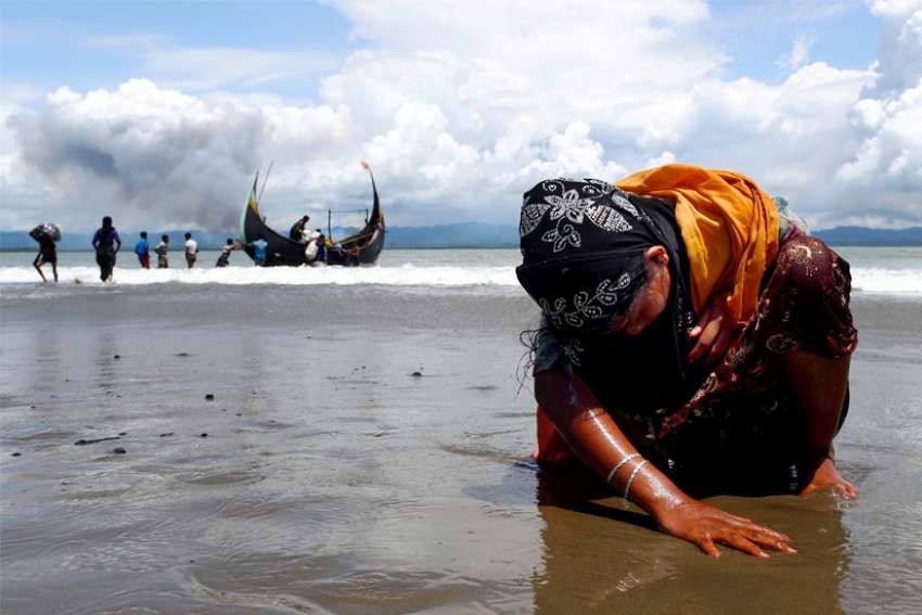 An exhausted Rohingya refugee woman touches the shore after crossing the Bangladesh-Myanmar border by boat through the Bay of Bengal in Shah Porir Dwip, Bangladesh, Sept. 11, 2017.