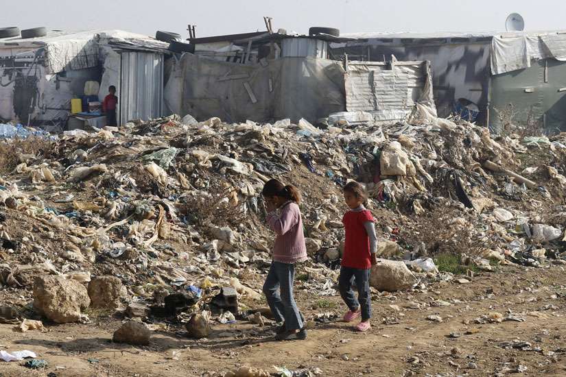 Syrian girls walk near garbage inside an informal refugee camp in Zahle, Lebanon.
