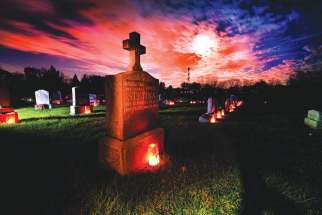 A grave marker of a couple is illuminated with a candle as a full moon shines through clouds on All Souls’ Day. The day, observed on Nov. 2, commemorates all the faithful who have died.