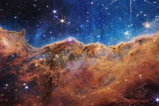 The &quot;Cosmic Cliffs&quot; of the Carina Nebula are seen in an image released by NASA July 12, 2022. The &quot;cliffs&quot; are divided horizontally by an undulating line between a cloudscape forming a nebula along the bottom portion and a comparatively clear upper portion. The image is from data provided by NASA&#039;s James Webb Space Telescope, a revolutionary apparatus designed to peer through the cosmos to the dawn of the universe. Speckled across both portions is a starfield, showing innumerable stars of many sizes.