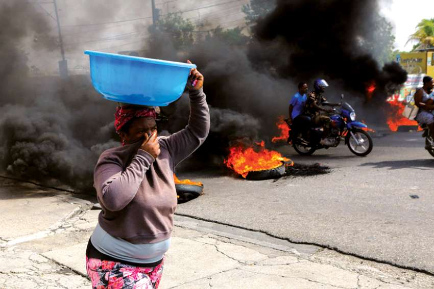 A woman covers her nose while walking past a burning road block as anger mounted over fuel shortages that have intensified as a result of gang violence in Port-au-Prince, Haiti, this past summer.