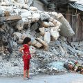 Girl stands in front of destroyed building in Syria, which is still home to one of the worst global crisis.