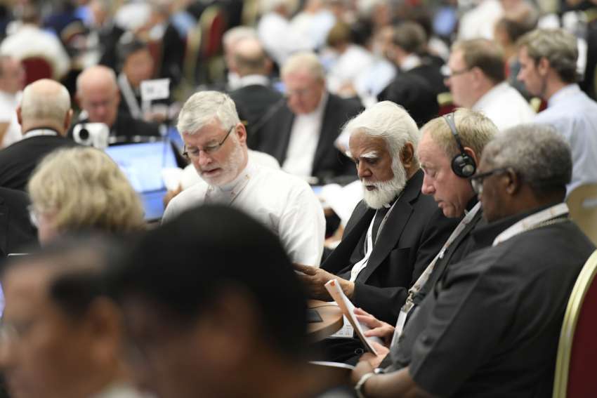Bishop Shane Mackinlay of Sandhurst, Australia, left, an elected member of the Commission for the Synthesis Report of the assembly of the Synod of Bishops, recites morning prayer with Cardinal Joseph Coutts, retired archbishop of Karachi, Pakistan, center, and Archbishop Michael Miller of Vancouver Oct. 12, 2023, in the Paul VI Audience Hall at the Vatican.