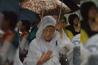 A woman prays with others in the rain outside Myongdong Cathedral in Seoul, South Korea, as Pope Francis celebrates a Mass for peace and for the reconciliation of North and South Korea inside Aug. 18. Many Catholic and non-Catholics braved the pouring ra in to try to get a glimpse of the pontiff at his last Mass before leaving South Korea. 