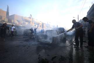 A man sprays water at the site of a car bomb blast in Qamishli, Syria, Oct. 11, 2019. Church bells have been ringing in Qamishli and elsewhere in northeastern Syria, signaling the alarm to Christians and others of the ongoing Turkish military operation having a devastating humanitarian impact on civilians.