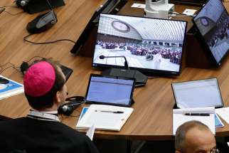 A bishop watches a video screen as his tablet with synod documents is open during the first session of the assembly of the Synod of Bishops in the Paul VI Audience Hall at the Vatican Oct. 4, 2023.