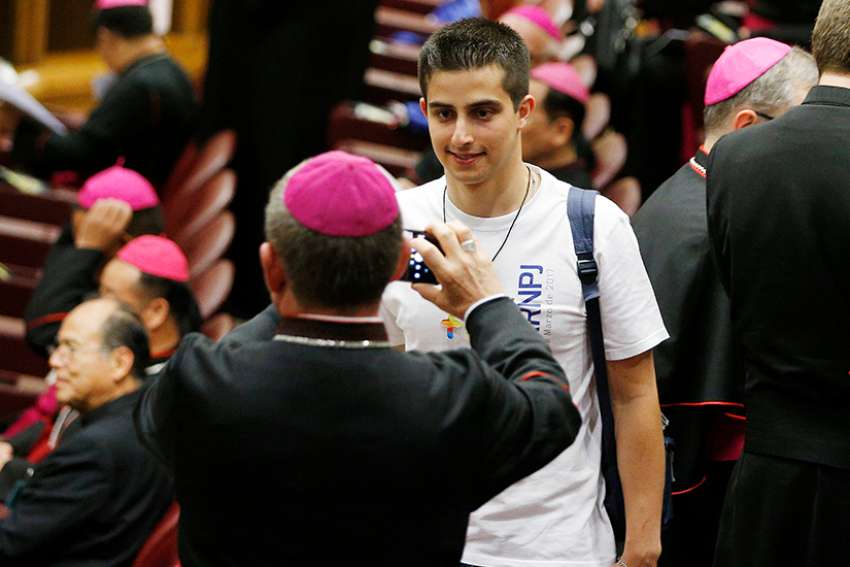  A bishop takes a photo of a youth delegate before the opening session of the Synod of Bishops on young people, the faith and vocational discernment at the Vatican Oct 3. 