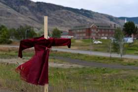 A child&#039;s red dress hangs on a stake near the grounds of the former Kamloops Indian Residential School June 6, 2021.