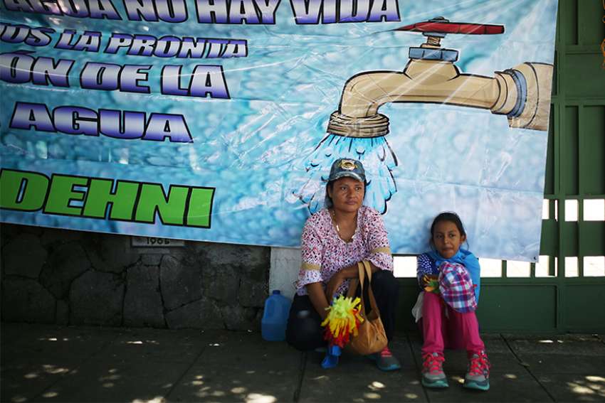 A woman and child sit in front of water poster in San Salvador, El Salvador, July 24, 2017