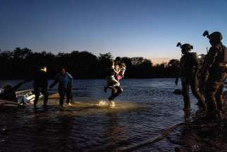 An asylum-seeking migrant carries two girls while walking in the Rio Grande as Texas Ranger officers await at the riverbank in Roma, Texas, April 5.
