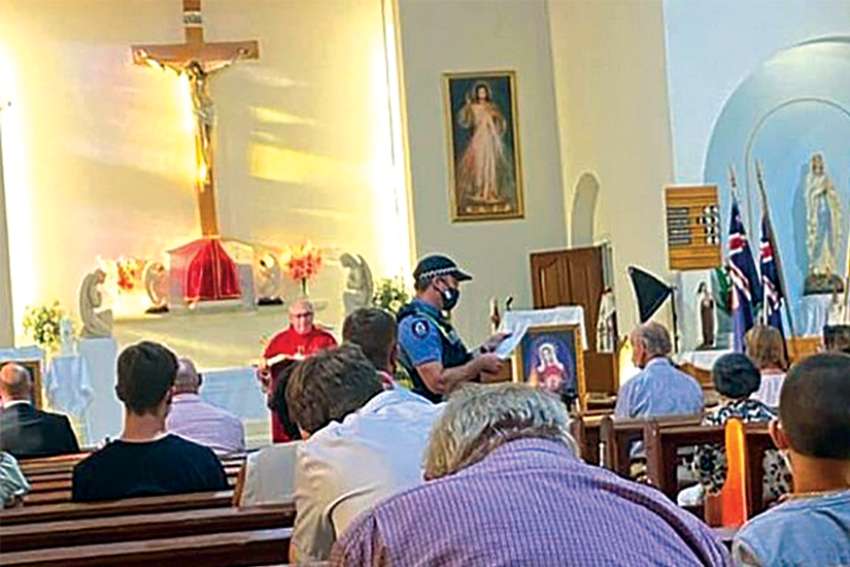 A police officer stops Mass at St. Bernadette’s Church in a suburb of Perth, Australia, Feb. 3 to make sure parishioners were wearing protective masks.
