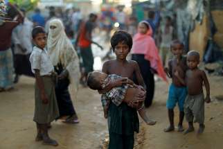 A young Rohingya refugee carries a child Oct. 10 while walking in a camp near Cox&#039;s Bazar, Bangladesh. Pope Francis, who will visit Bangladesh Nov. 30-Dec. 2, has appealed for their protection of the Rohingya on several occasions, calling them &quot;our brothers and sisters.&quot;
