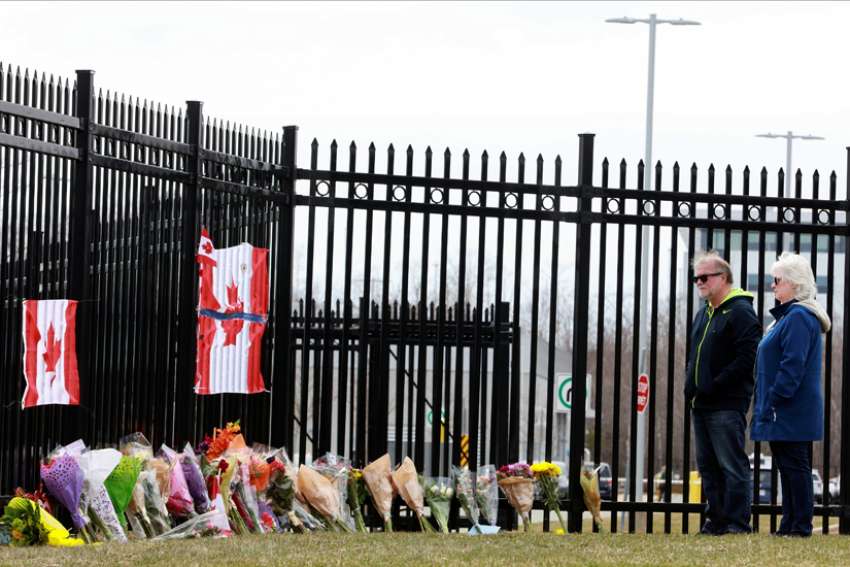 A man and woman stand before a makeshift memorial at the Royal Canadian Mounted Police headquarters in Dartmouth, Nova Scotia, April 20, 2020. The previous day, a shooter went on a 12-hour rampage that left at least 19 people dead.