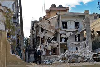 Residents walk past a destroyed building in 2014 after airstrikes in Aleppo, Syria. Pope Francis says the war-torn country needs a political solution not a military one. 