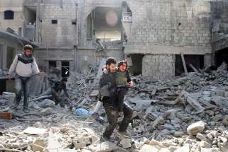 A man carries an injured boy amid destroyed buildings Feb. 21 in rebel-held Eastern Ghouta, a suburb of Damascus, Syria.