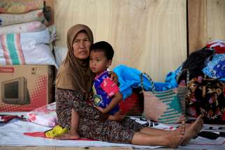  A woman holds her son as they rest Oct. 3 outside their damaged home after an earthquake hit Indonesia&#039;s Sulawesi island.