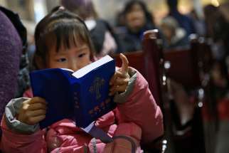 A girl looks at a Bible during Mass in 2016 at a Beijing cathedral. As young people move to cities, Catholic grandparents in rural areas are passing on the faith to their grandchildren.