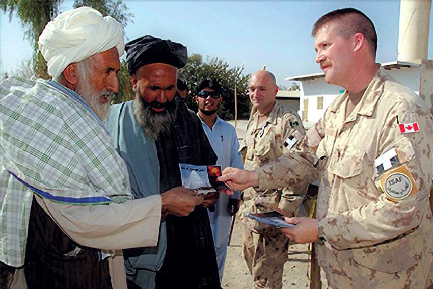 Padre Murray Bateman (right) and Major Luis Cavallo (in background) offer Afghan men cards wishing them Eid Mubarek or “Blessed Eid” after they are welcomed to Camp Nathan Smith, Kandahar, Afghanistan in 2008.