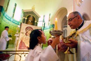 An altar girl receives the Eucharist from a priest.
