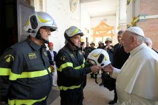 A firefighter hands Pope Francis a fire helmet made specifically for him to wear June 16, 2019, as he visits the Camerino cathedral, which suffered major damage during an earthquake in October 2016.