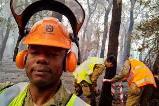 Father Kene Onwukwe, assistant pastor of Sacred Heart Church in Mosman, Australia, poses as he and other men prepare to cut down a tree damaged by a bushfire in Wonboyn Jan. 13, 2020. Father Onwukwe is a chaplain with the army reserve currently working full time alongside soldiers supporting exhausted firefighters in the bushfire relief efforts.