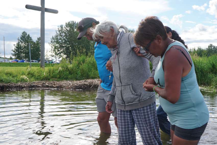 Mary Agnes Herman is helped out of Lac Ste. Anne at the 2018 pilgrimage.